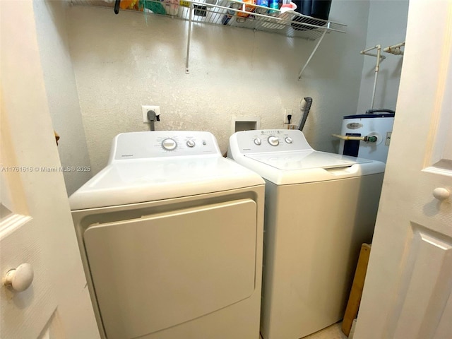 washroom with laundry area, washing machine and dryer, water heater, and a textured wall