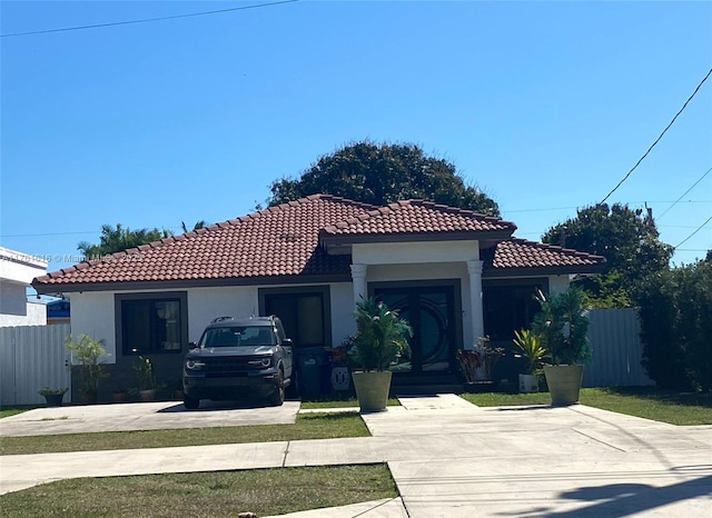 mediterranean / spanish-style house featuring a tile roof, stucco siding, concrete driveway, and fence