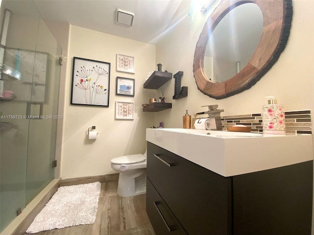 bathroom featuring vanity, baseboards, a shower stall, toilet, and tasteful backsplash