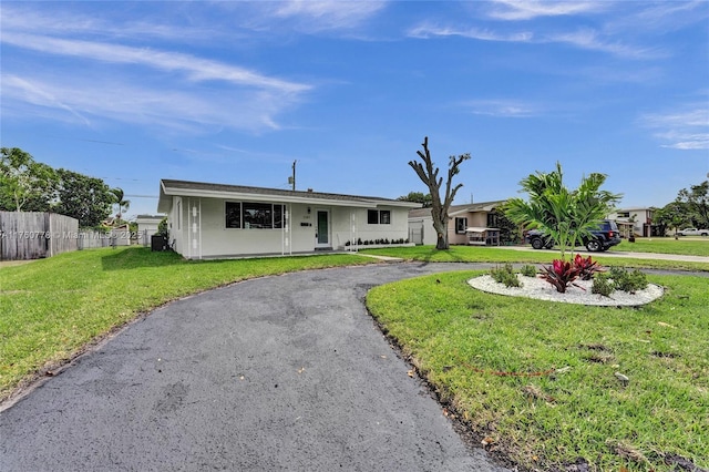 ranch-style house with a front lawn, fence, driveway, and stucco siding