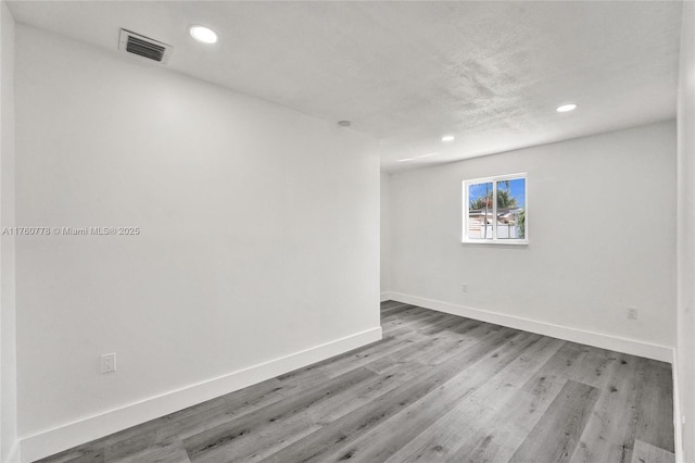 empty room with recessed lighting, wood finished floors, visible vents, and baseboards