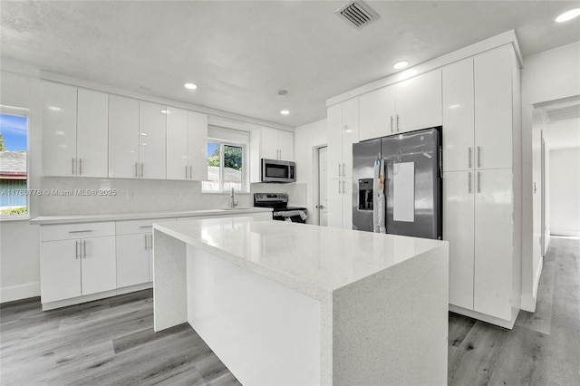 kitchen featuring light wood finished floors, visible vents, stainless steel appliances, modern cabinets, and a sink