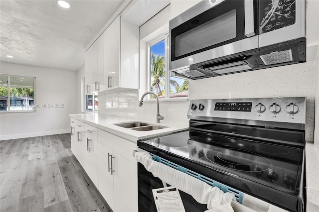 kitchen featuring tasteful backsplash, appliances with stainless steel finishes, light wood-style floors, white cabinets, and a sink