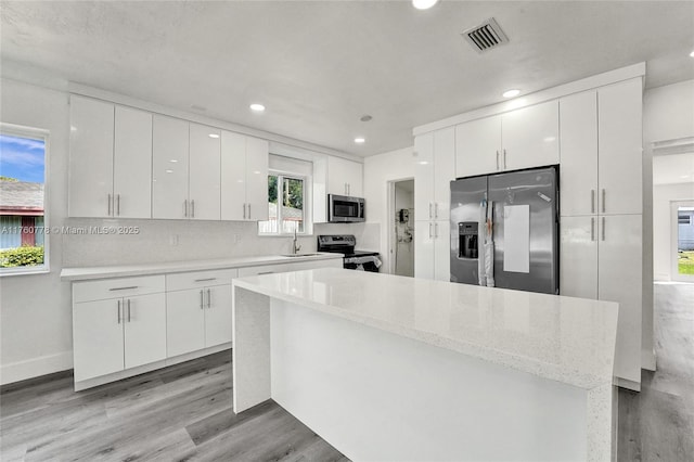 kitchen with visible vents, light wood finished floors, a sink, stainless steel appliances, and modern cabinets