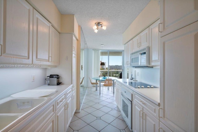 kitchen with light countertops, a textured ceiling, light tile patterned floors, white appliances, and white cabinetry