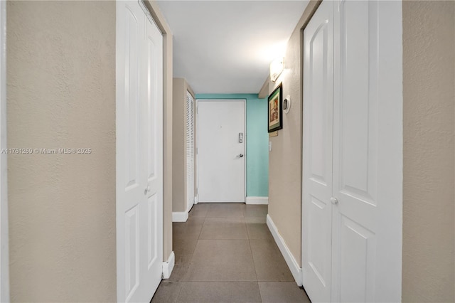 hallway featuring tile patterned floors, baseboards, and a textured wall