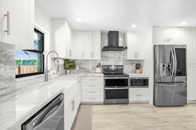 kitchen featuring white cabinetry, light stone counters, wall chimney exhaust hood, and appliances with stainless steel finishes