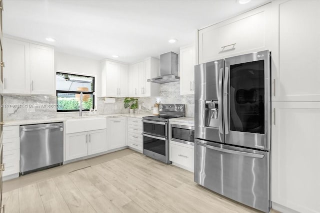 kitchen featuring backsplash, wall chimney range hood, light wood-style flooring, appliances with stainless steel finishes, and white cabinetry