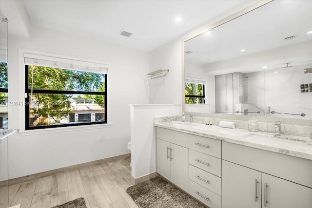 bathroom with toilet, a stall shower, a sink, wood finished floors, and double vanity