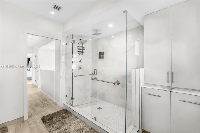 full bath featuring a marble finish shower, visible vents, recessed lighting, and wood finished floors