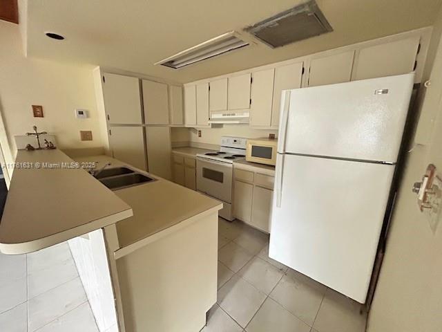 kitchen featuring under cabinet range hood, light countertops, light tile patterned floors, white appliances, and a sink