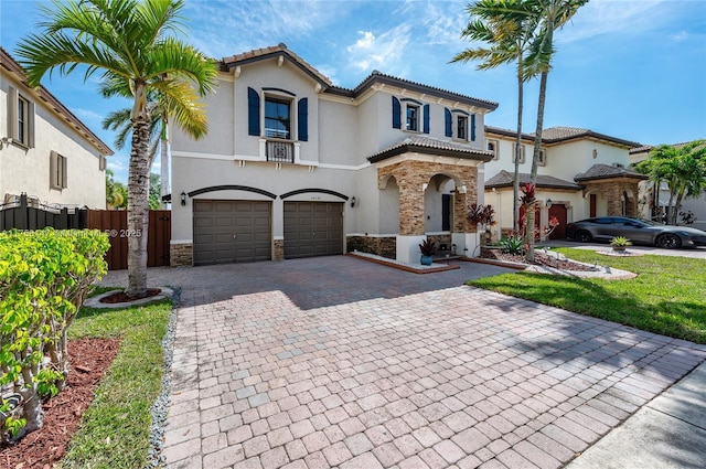 mediterranean / spanish-style home featuring fence, stucco siding, decorative driveway, stone siding, and an attached garage