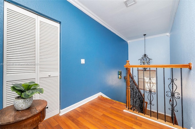 hall featuring visible vents, crown molding, baseboards, an upstairs landing, and wood finished floors