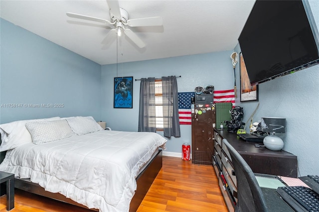 bedroom with a textured wall, a ceiling fan, baseboards, and wood finished floors