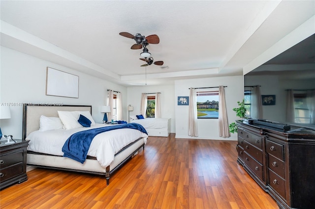 bedroom with a ceiling fan, a raised ceiling, wood finished floors, and baseboards