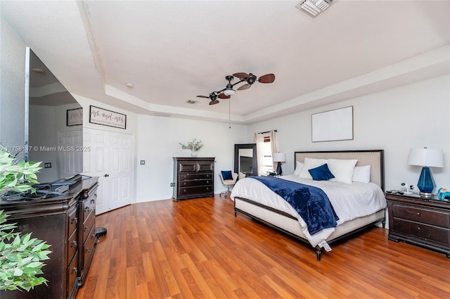 bedroom featuring light wood-type flooring, visible vents, a raised ceiling, and a ceiling fan