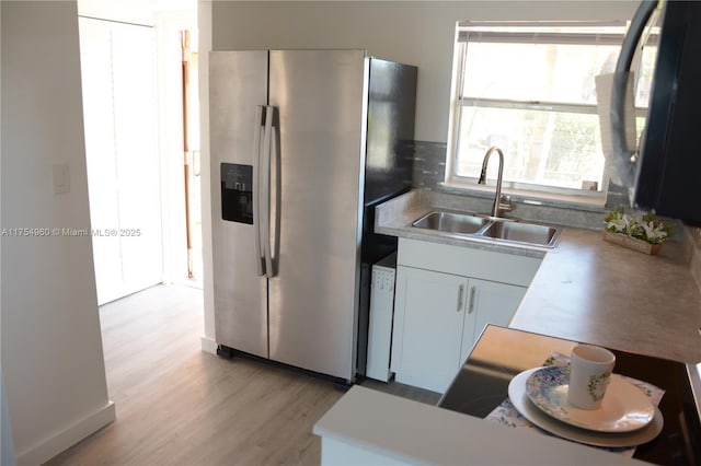 kitchen with stainless steel fridge, light countertops, light wood-type flooring, and a sink