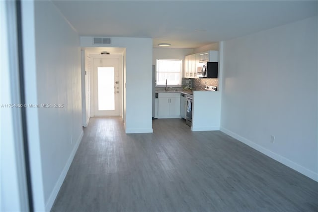 unfurnished living room featuring a sink, wood finished floors, visible vents, and baseboards