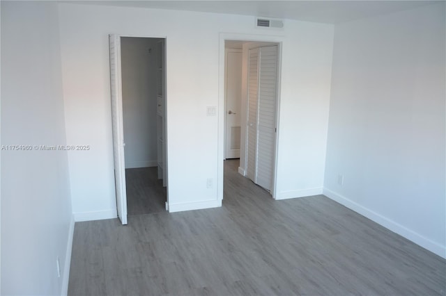 unfurnished bedroom with a spacious closet, a closet, baseboards, and wood finished floors