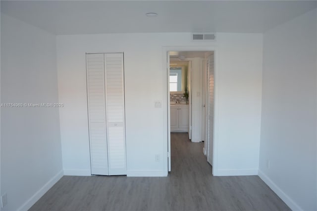 unfurnished bedroom featuring visible vents, baseboards, a closet, and wood finished floors