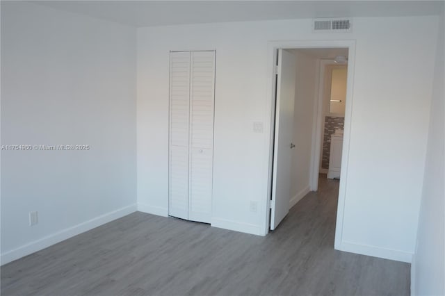 unfurnished bedroom featuring wood finished floors, visible vents, a closet, and baseboards