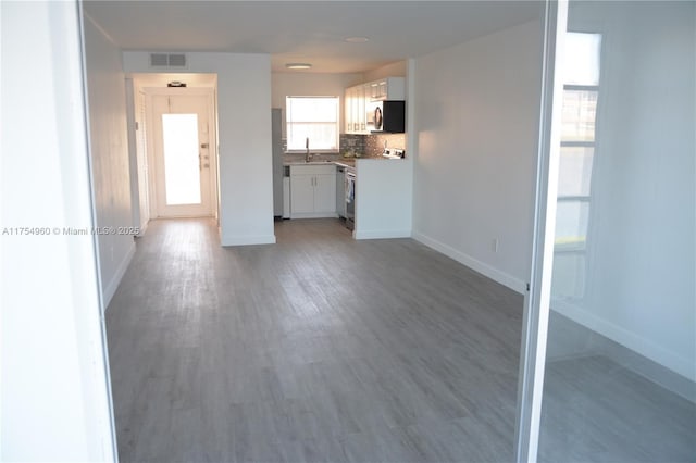 unfurnished living room with a sink, light wood-style floors, visible vents, and baseboards