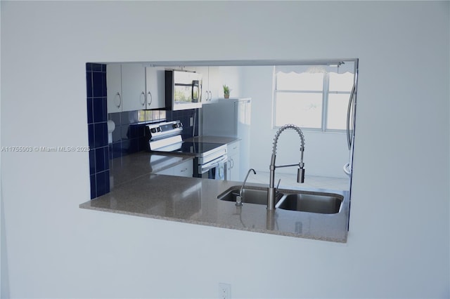 kitchen with stainless steel electric stove, stone countertops, backsplash, and a sink