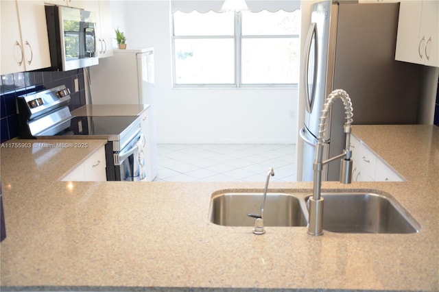 kitchen with a sink, tasteful backsplash, appliances with stainless steel finishes, white cabinets, and tile patterned flooring