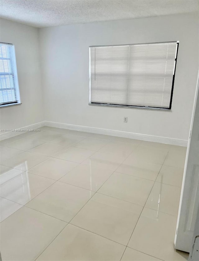 spare room featuring tile patterned floors, baseboards, and a textured ceiling