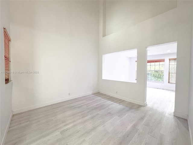 spare room featuring a high ceiling, light wood-type flooring, and baseboards