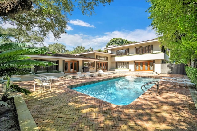 rear view of house featuring a patio, a balcony, an outdoor pool, stucco siding, and french doors