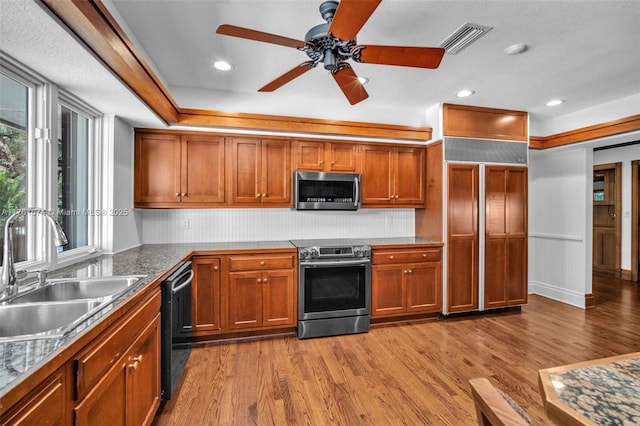 kitchen featuring visible vents, brown cabinets, wood finished floors, stainless steel appliances, and a sink