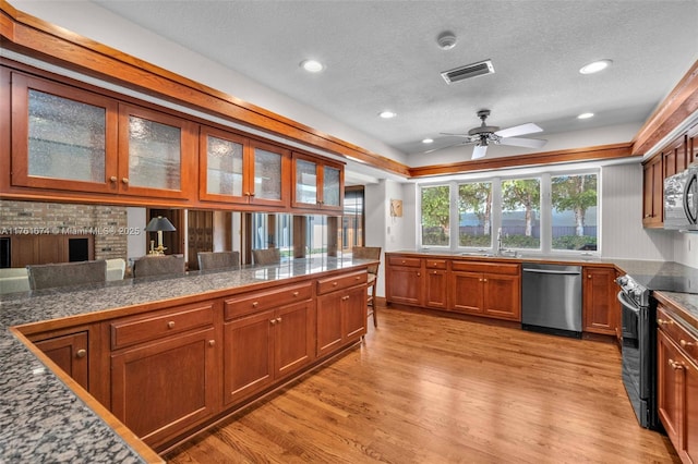 kitchen with stainless steel dishwasher, black range with electric cooktop, visible vents, light wood-style floors, and brown cabinets