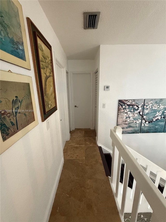 hallway featuring visible vents, baseboards, and a textured ceiling