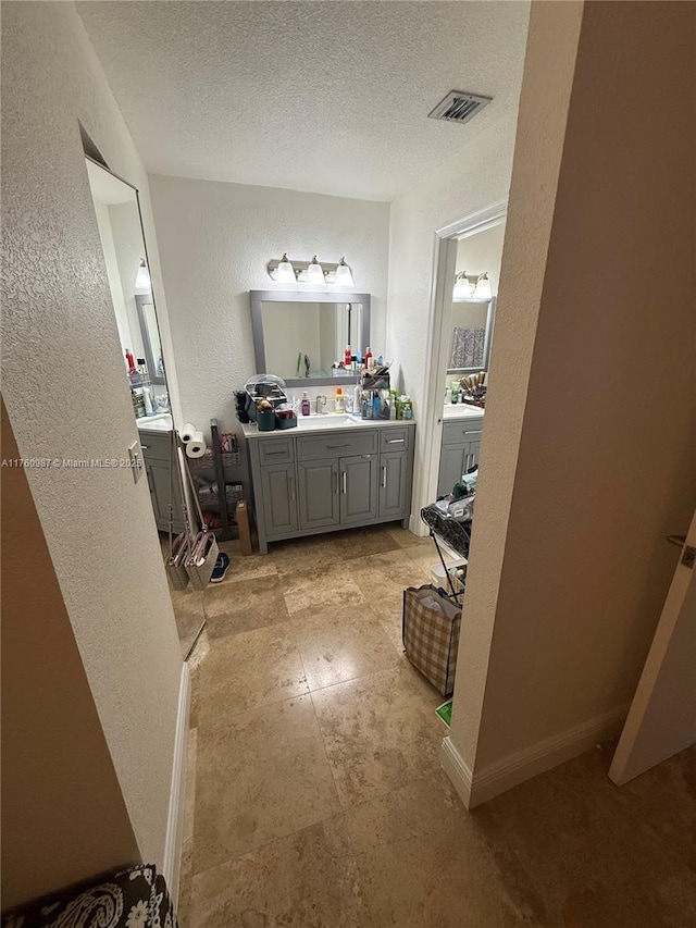 bathroom with visible vents, a textured ceiling, vanity, and a textured wall