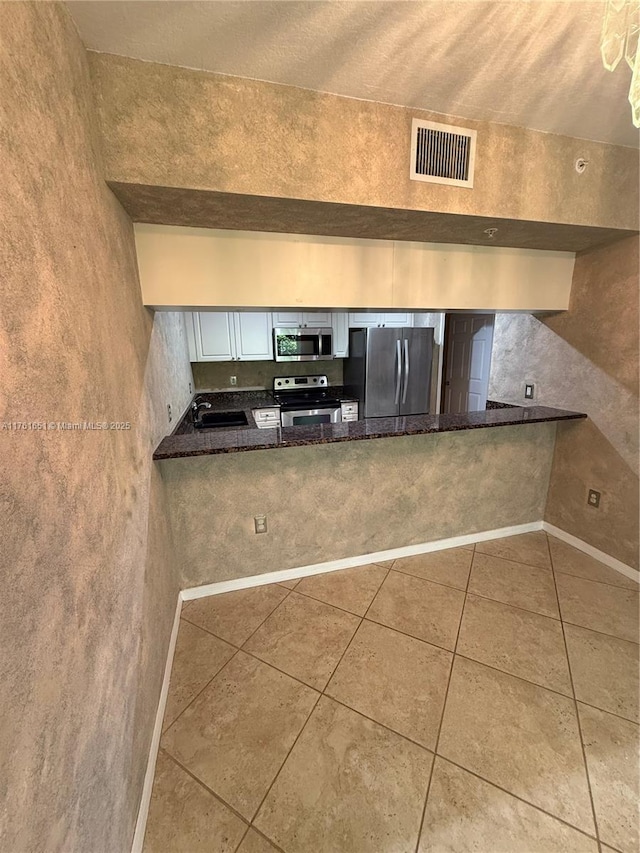 kitchen with tile patterned flooring, visible vents, appliances with stainless steel finishes, a peninsula, and white cabinetry