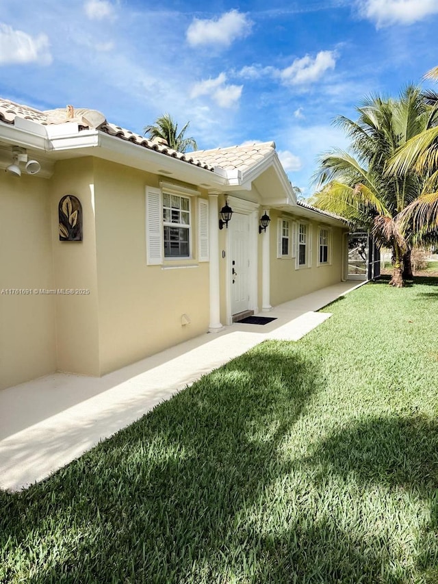 exterior space featuring stucco siding, a yard, and a tiled roof