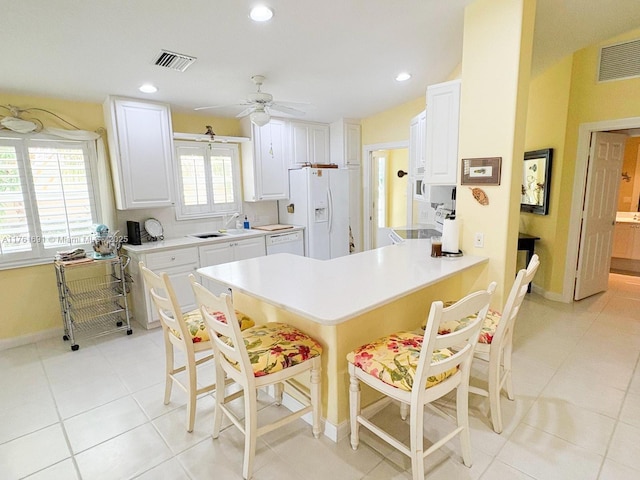 kitchen with white appliances, a kitchen breakfast bar, a peninsula, and visible vents