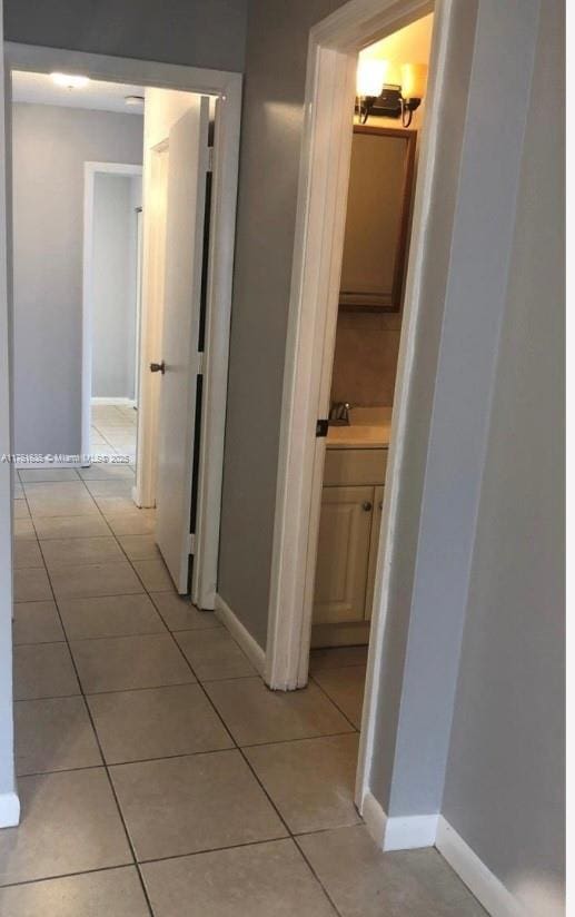 corridor with a sink, baseboards, and light tile patterned flooring