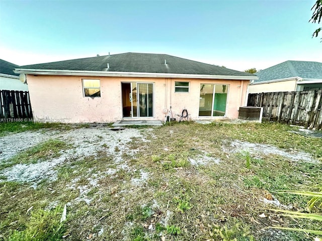 rear view of house with stucco siding and fence