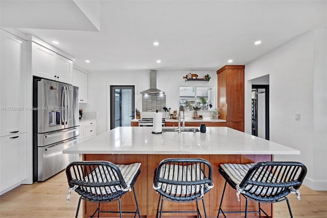 kitchen with stainless steel fridge with ice dispenser, a sink, light countertops, wall chimney range hood, and light wood-type flooring