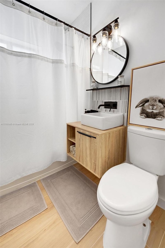 bathroom featuring shower / bathtub combination with curtain, toilet, vanity, and wood finished floors