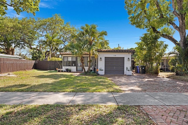 view of front facade featuring a front yard, decorative driveway, fence, and a garage