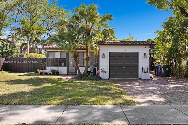 view of front facade with a front yard, fence, a garage, a tile roof, and decorative driveway