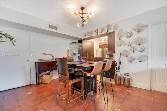 dining area with visible vents, a textured ceiling, an inviting chandelier, light tile patterned flooring, and baseboards