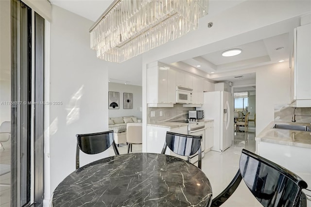 kitchen with white appliances, light countertops, white cabinetry, a raised ceiling, and backsplash