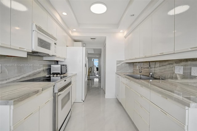 kitchen featuring tasteful backsplash, white appliances, white cabinetry, a raised ceiling, and a sink