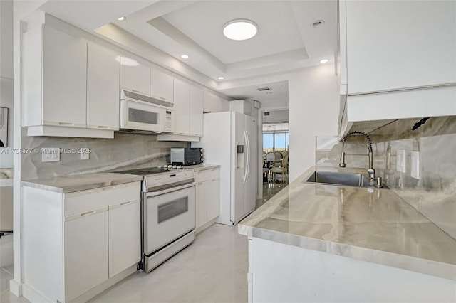 kitchen featuring white appliances, a sink, stainless steel countertops, a raised ceiling, and tasteful backsplash