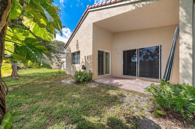 back of house with stucco siding, a lawn, a tile roof, and a patio area