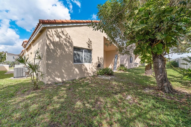 view of side of property with a tile roof, a yard, central AC unit, and stucco siding